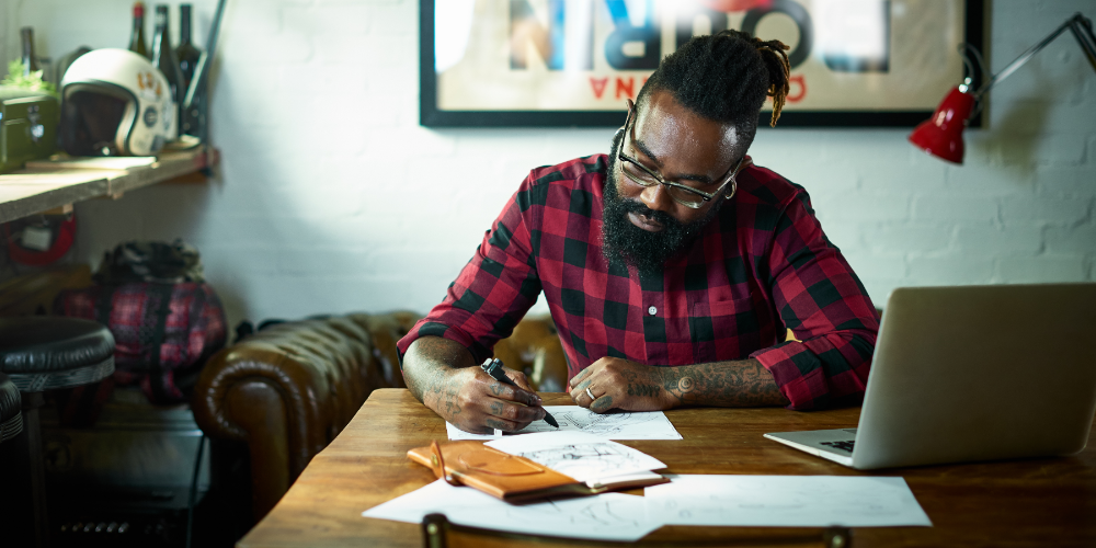 Male designer with tattoos drawing at desk.