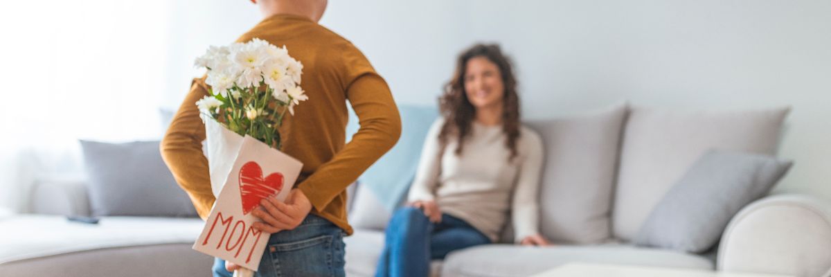 Happy mother's day! Child son congratulates moms and gives her a postcard. Child boy congratulates mother and gives a bouquet of flowers and gift