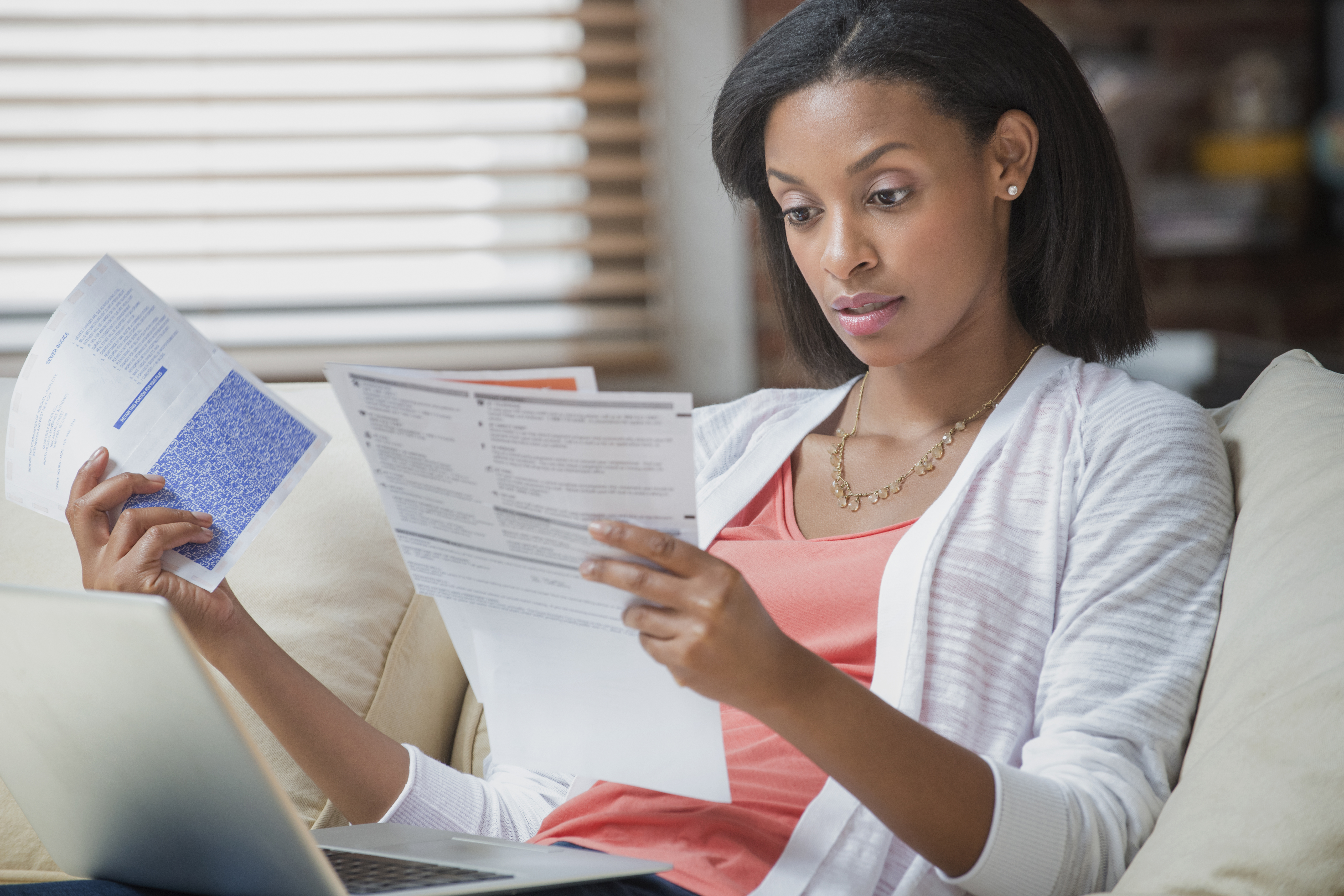 Mixed race woman reading bills on sofa