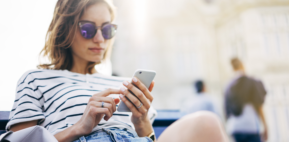 Hipster envoyant un message sur un smartphone ou autre appareil technologique, représentation d'un écran blanc. Jeune femme utilisant un téléphone portable, château en arrière‑plan. Mains d'une touriste tenant un gadget, arrière‑plan flou aux nuances estivales