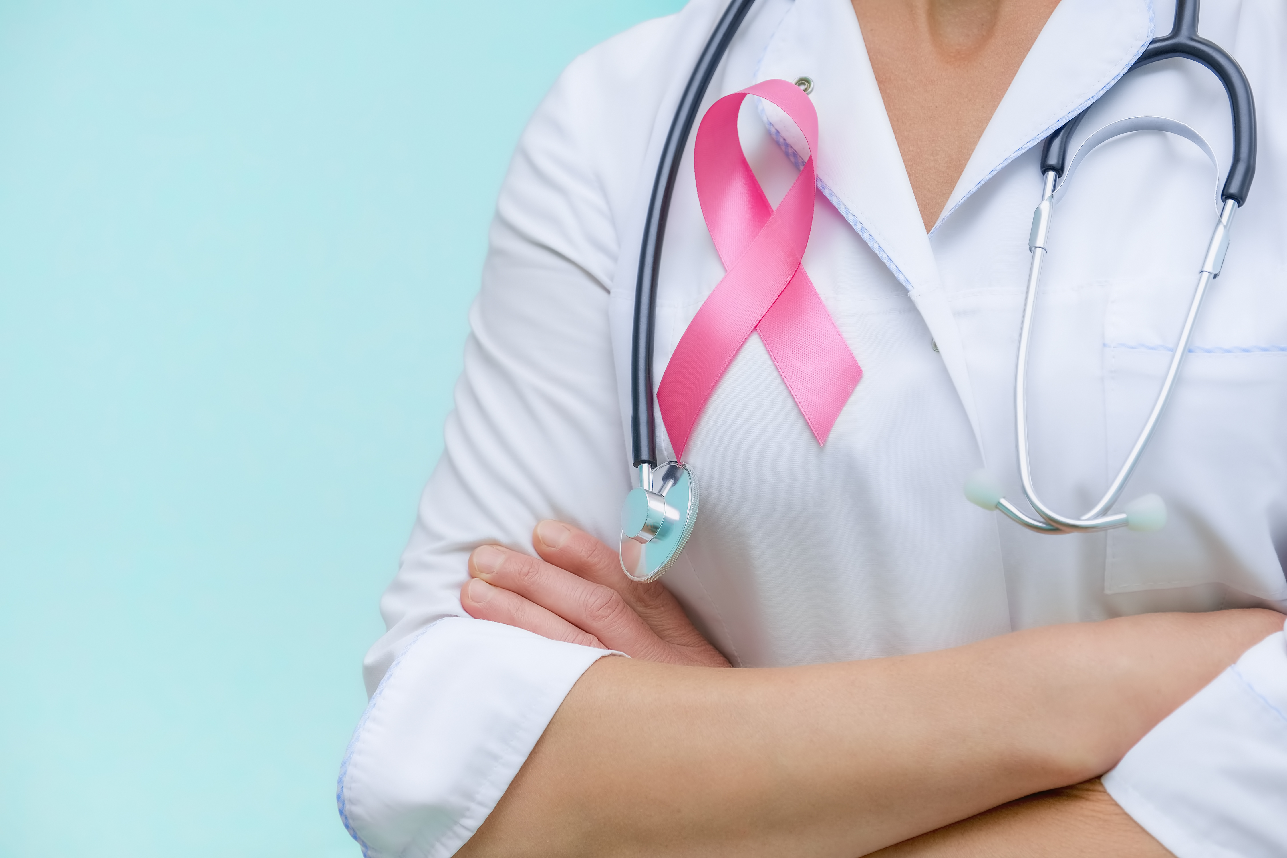 Doctor with folded arms and a stethoscope on his neck, shows a pink ribbon close-up on uniform on a blue background.