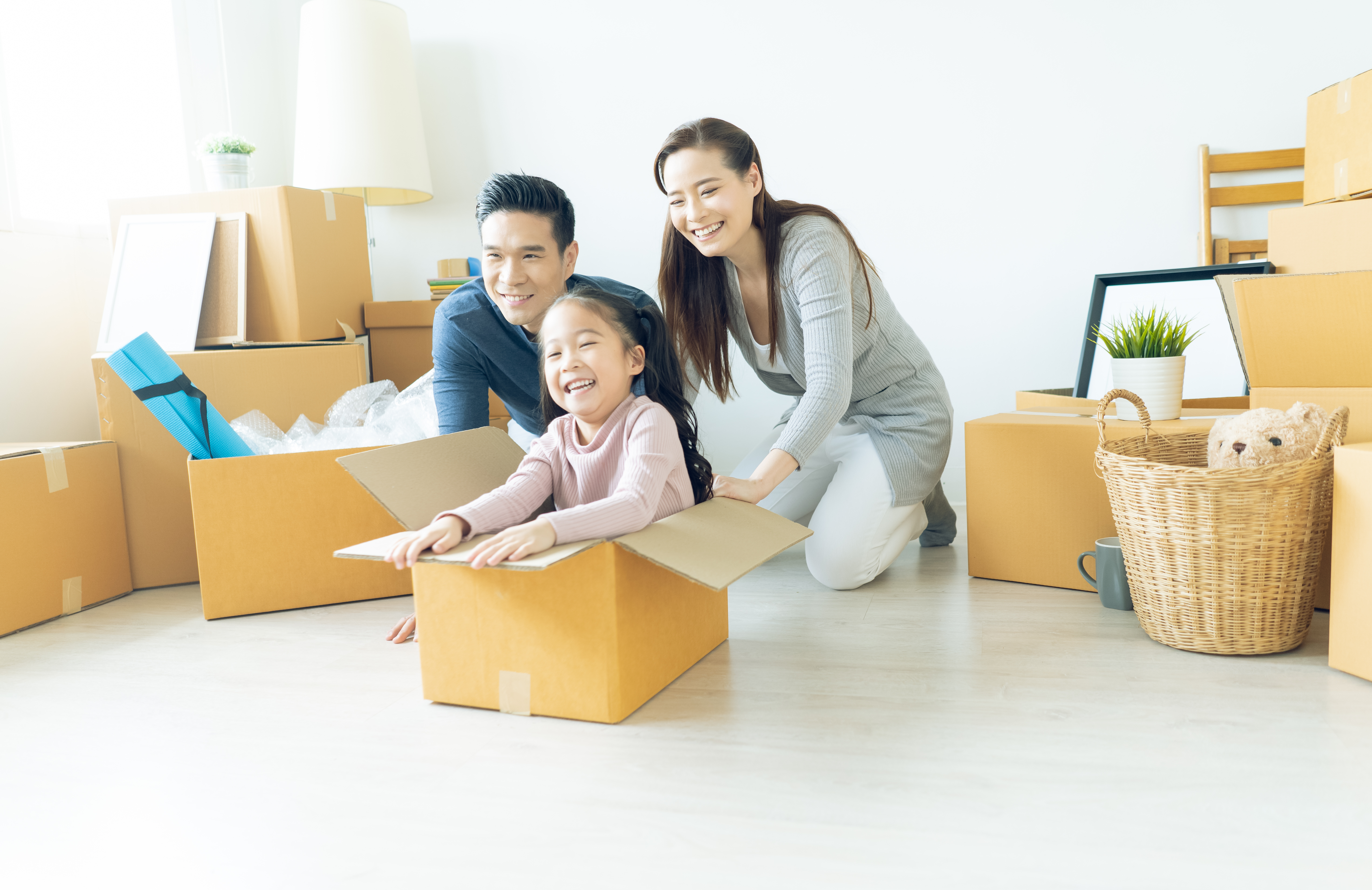 Happy young Asian family of three having fun moving with cardboard boxes in new house at moving day. Moving house day and express delivery concept.