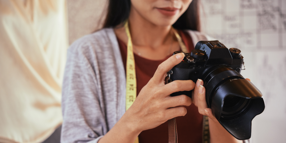 Unrecognizable fashion designer holding professional camera and looking at pictures of outfit on it