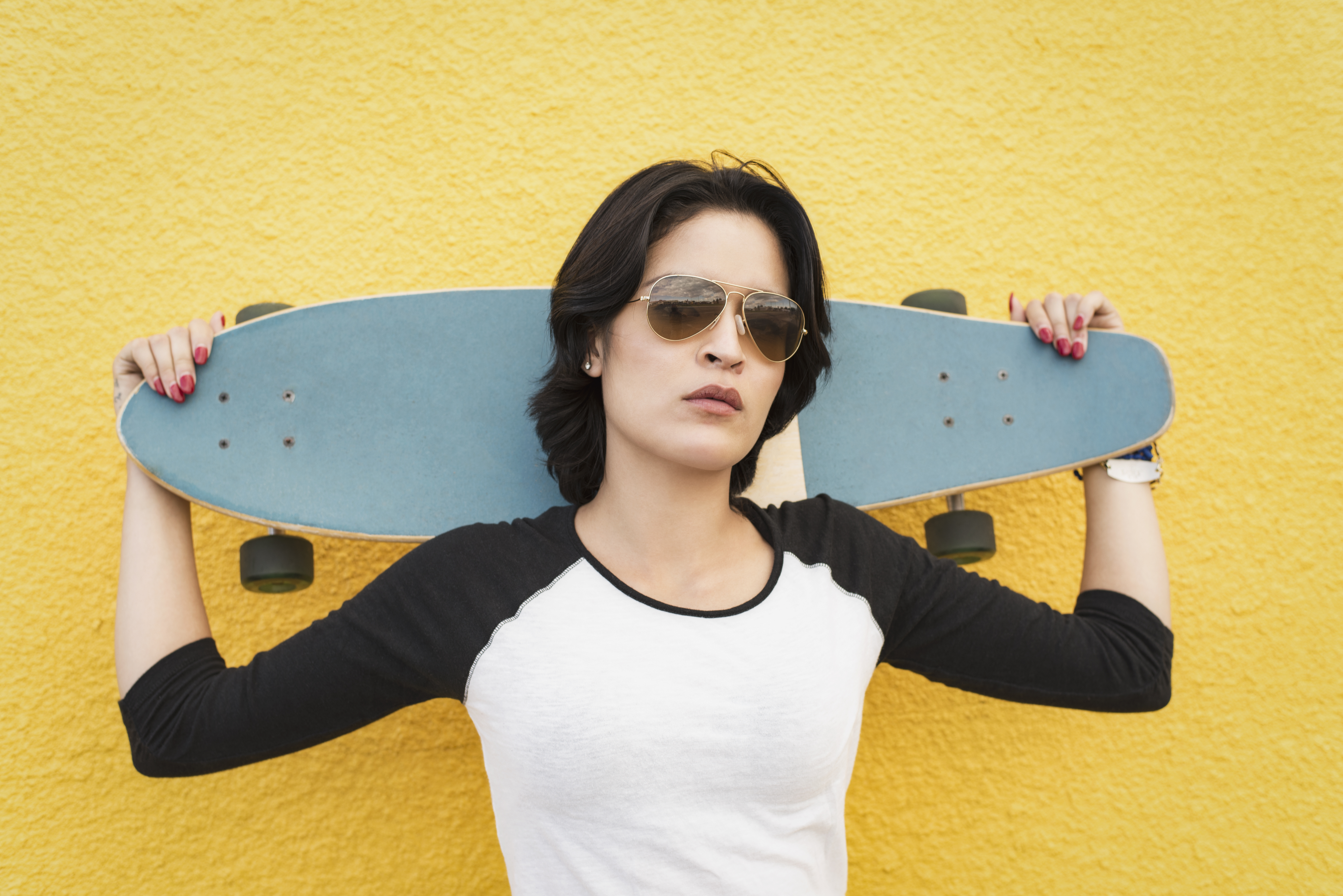 Jonge latina vrouw met skateboard voor een gele muur 