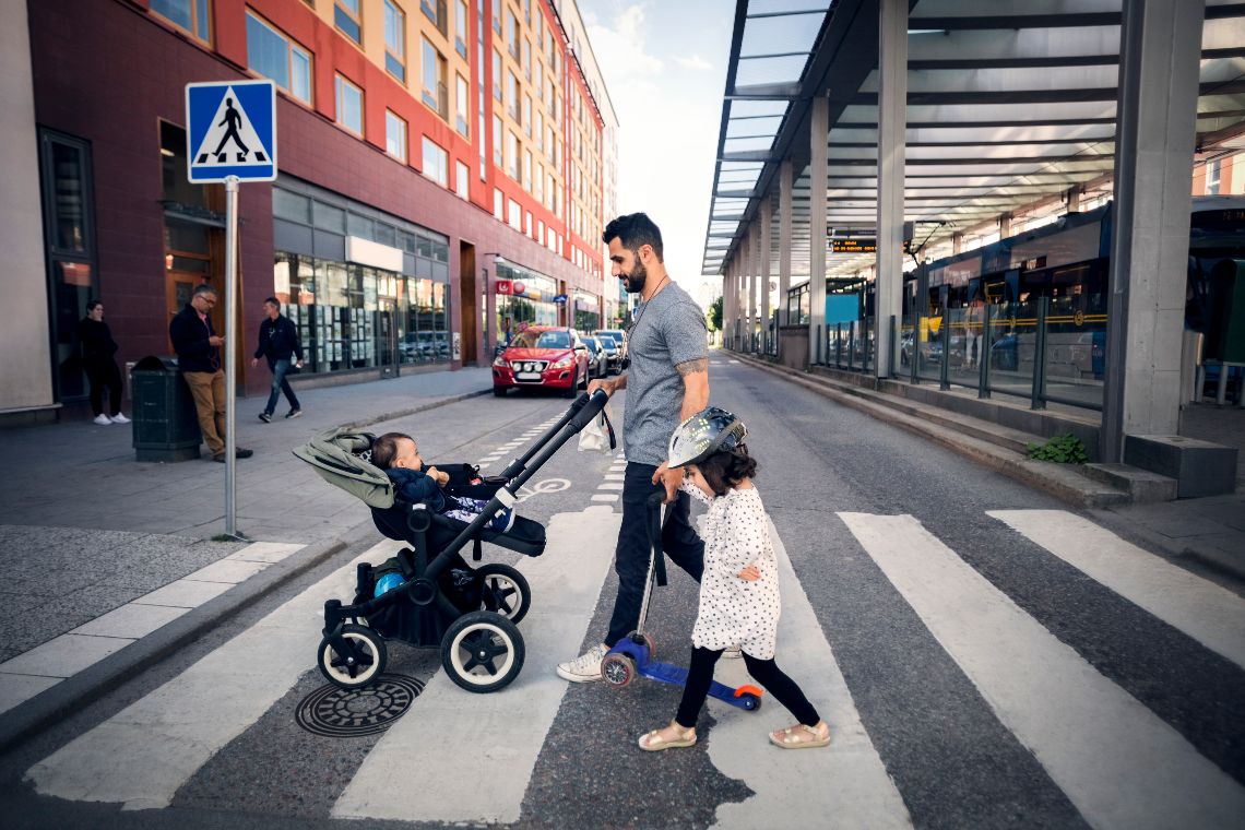 Side view of father crossing street with daughter while holding baby stroller in city