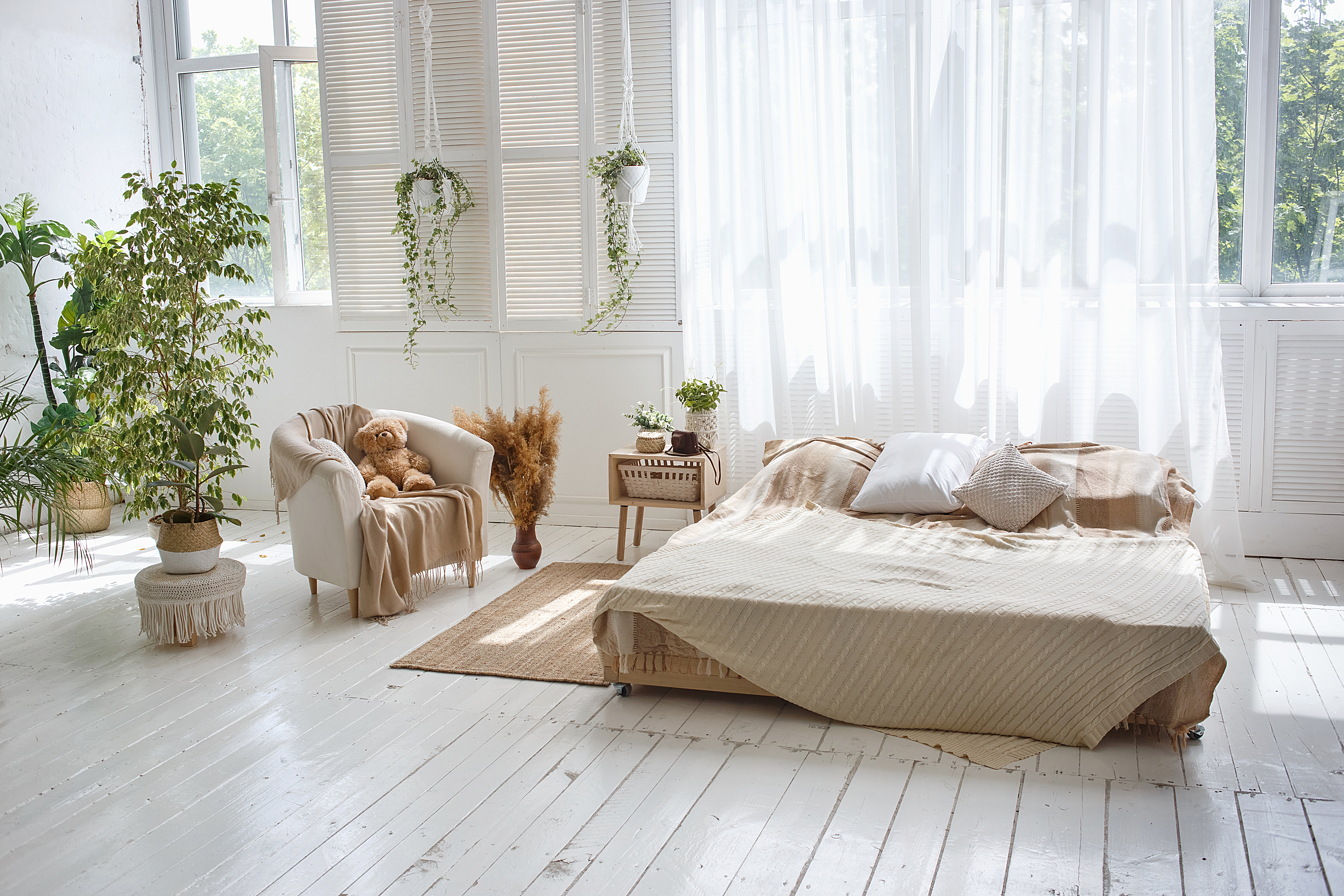 Stylish bright loft cozy room with double bed, armchair, green plants, curtains, white brick walls and wooden floor.