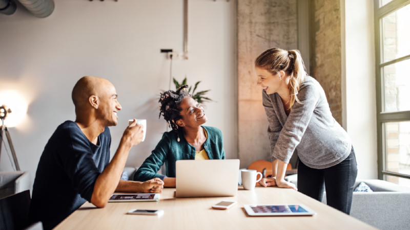 Business colleagues talking while using laptop at office