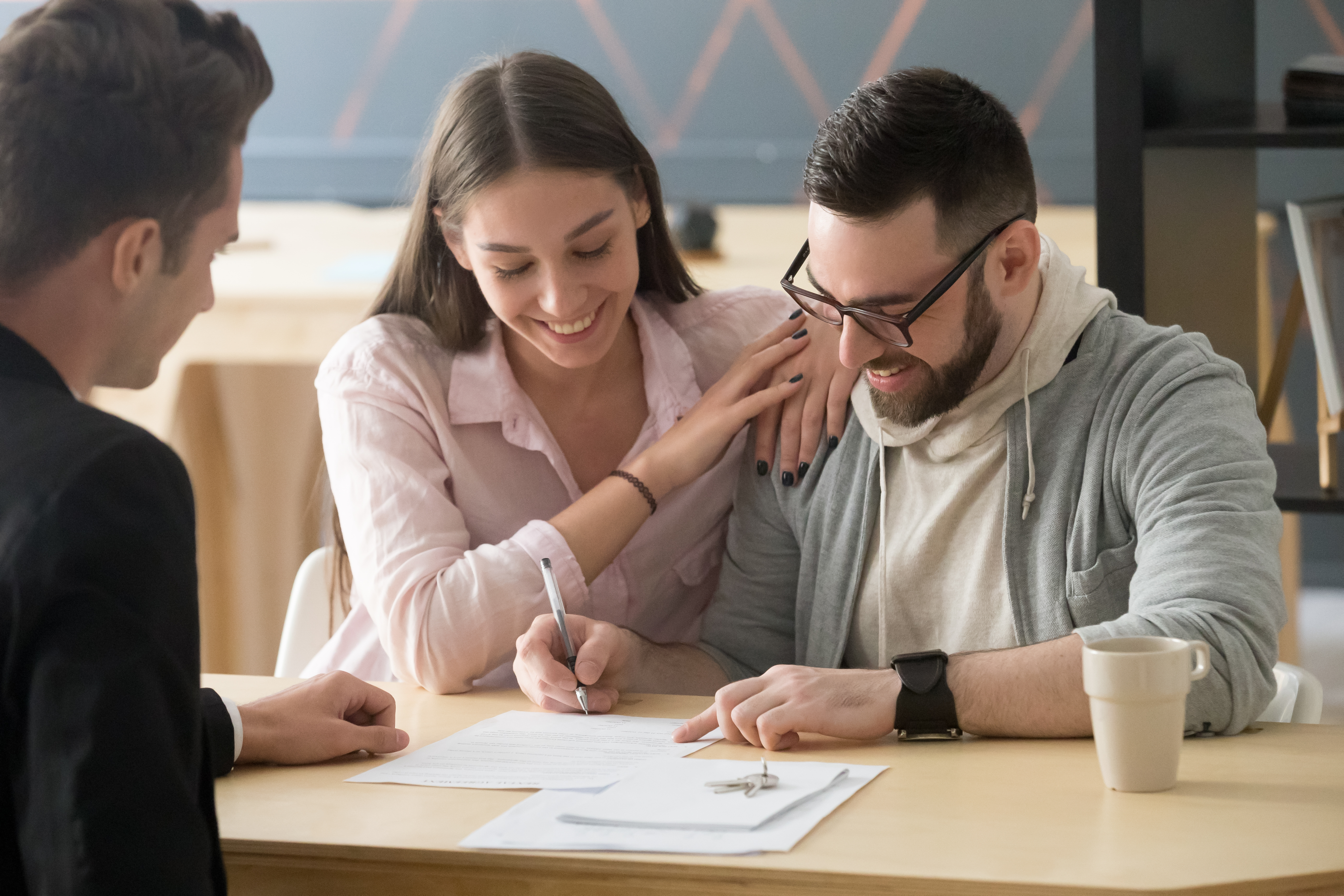 Excited couple sign purchase contract in realtor office