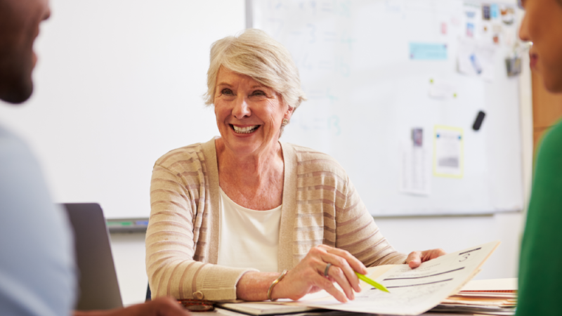 Senior teacher at desk talking to adult education students