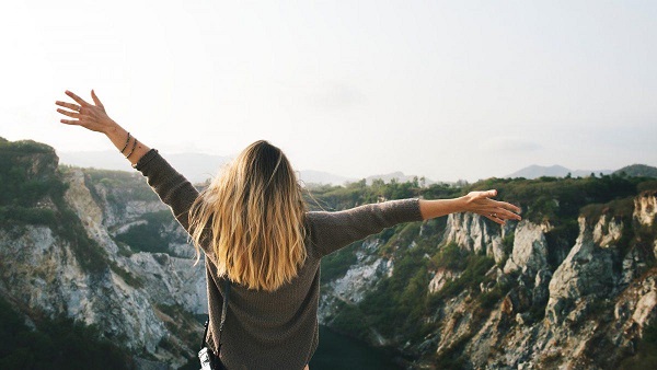 Woman with outstretched arms overlooking a mountain cliff