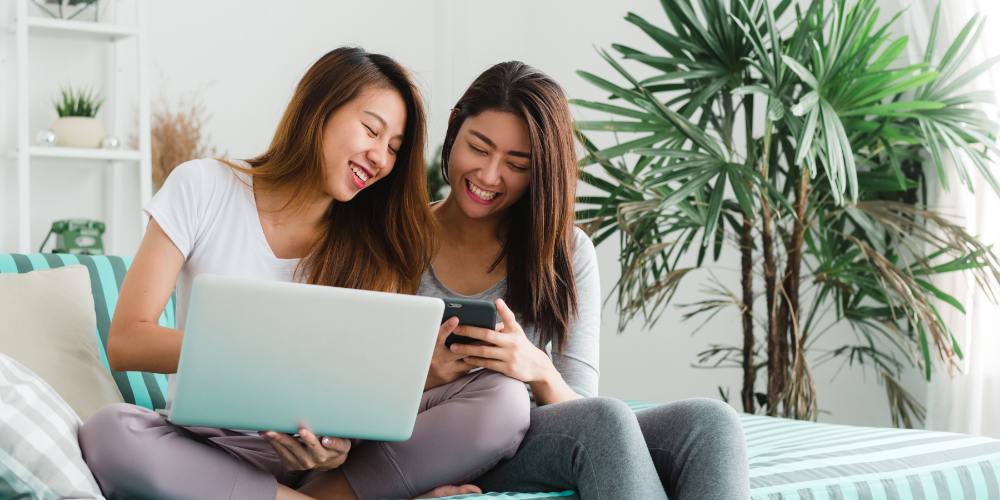 Beautiful young asian women LGBT lesbian happy couple sitting on sofa buying online using laptop a computer and phone in living room at home. LGBT lesbian couple together indoors concept.