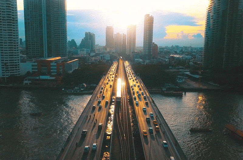 An aerial view of a bridge in Bangkok with the sun setting in the background 